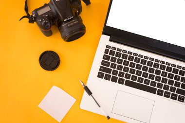 İş yerindeki fotoğrafçılar sarı arka planda. Laptop, dijital kamera, lens, hafıza kartı, çıkartmalar Minimalizm. Yukarıdan bak. Fotoğrafçı için uzay ekipmanlarını kopyala. Serbest konsept