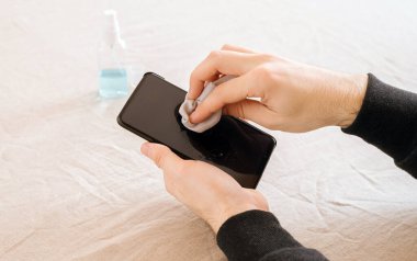 Erkeklerin elleri antiseptik ıslak mendille telefonu temizliyor. Coronavirus küresel salgını. Halka açık yerleri ziyaret ettikten sonra koronavirüsün önlenmesi. Odaklanma.