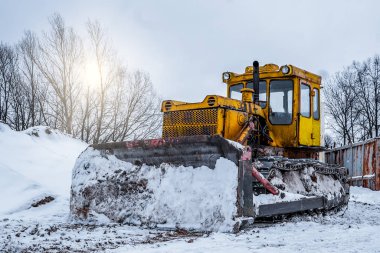Yeni inşaat alanında sarı kazıcı, parlak güneş ve arka planda güzel mavi gökyüzü. Kışın sokakta sarı buldozer, kar yağışı ve kar yamaçları.