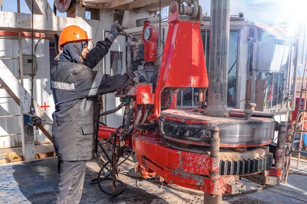 Kırmızı üniformalı, miğferli ve gözlüklü matkapçı. Petrol kuyusuna indirmek için matkap borularını vidalamak ve delmeye devam etmek için hidrolik anahtar kullanıyor. Çalışan insan kavramı.