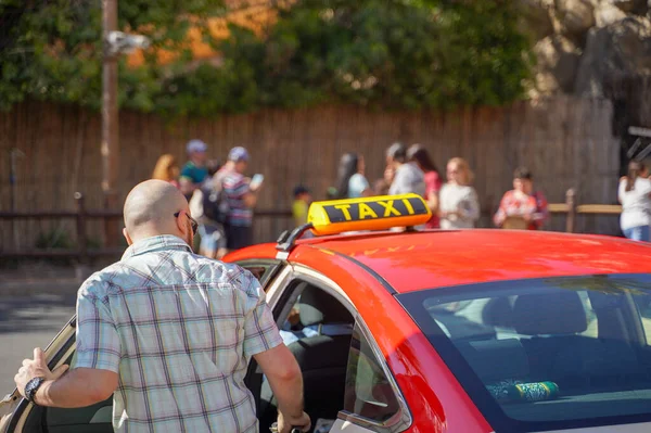 Bild eines jungen Mannes mit Schirmmütze und kariertem Hemd, der auf dem Rücksitz im gelben Taxi sitzt. Glücklicher Mann beim Einsteigen in ein Taxi. Geschäftsmann steigt auf der Stadtstraße in ein Taxi. — Stockfoto