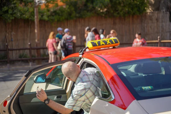 Bild eines jungen Mannes mit Schirmmütze und kariertem Hemd, der auf dem Rücksitz im gelben Taxi sitzt. Glücklicher Mann beim Einsteigen in ein Taxi. Geschäftsmann steigt auf der Stadtstraße in ein Taxi. — Stockfoto