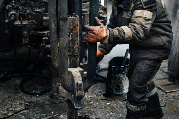 Kırmızı üniformalı, miğferli ve gözlüklü matkapçı. Petrol kuyusuna indirmek için matkap borularını vidalamak ve delmeye devam etmek için hidrolik anahtar kullanıyor. Çalışan insan kavramı.