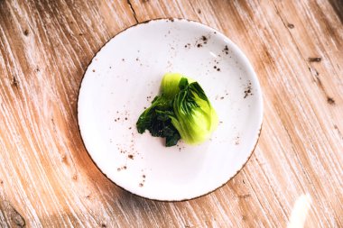 Ahşap bir arka planda seramik bir tabakta pişirilmiş bok choy.