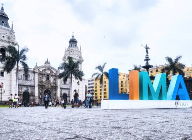 Lima, Peru - 28 Ocak 2020: Kasabanın merkezi olan Plaza Mayor 'daki Lima tabelasında poz veren turistler, yayalar ve sakinler. Basilica Katedrali en sonda.