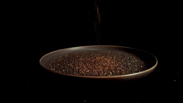 bright dry chia seeds pour onto dark turning plate on black background extreme close view