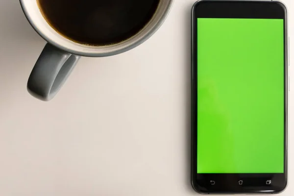 Chytrý telefon s zelenou obrazovkou vedle šálek kávy — Stock fotografie