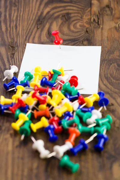 Various color thumbtacks and note on distressed wood — Stock Photo, Image