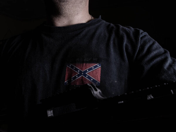 Anonymous man wearing confederate flag t-shirt holding gun