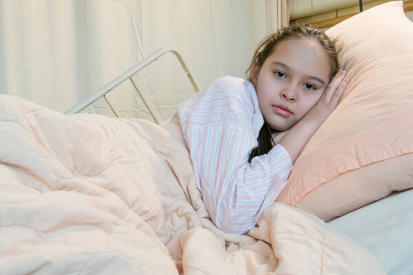 Mixed race tween girl in hospital bed, looking at camera