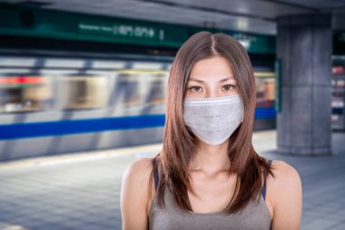 Arka planda çözülmüş Taipei metro istasyonu olan cerrahi maske takan Çinli bir kadın.