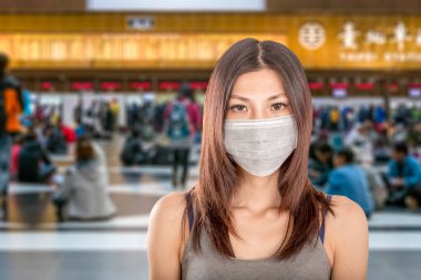 Arka planda çözülmüş Taipei tren istasyonu olan cerrahi maske takan Çinli bir kadın.