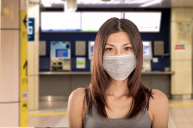 Arka planda Japon metro istasyonuna odaklanmış cerrahi maske takan Çinli kadın.