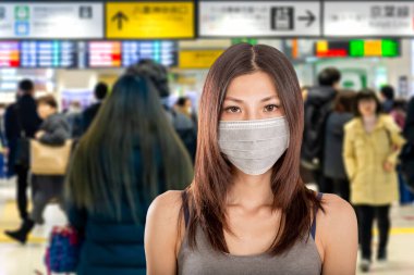 Arka planda Japon metro istasyonuna odaklanmış cerrahi maske takan Çinli kadın.