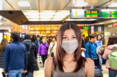 Arka planda Japon metro istasyonuna odaklanmış cerrahi maske takan Çinli kadın.