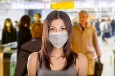 Arka planda Japon metro istasyonuna odaklanmış cerrahi maske takan Çinli kadın.