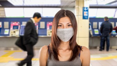 Arka planda Japon metro istasyonuna odaklanmış cerrahi maske takan Çinli kadın.