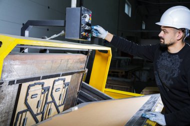 Sert şapkalı bir işçi yumruk makinesini çalıştırıyor. Karton kutu fabrikası. Kağıt kesme makinesi