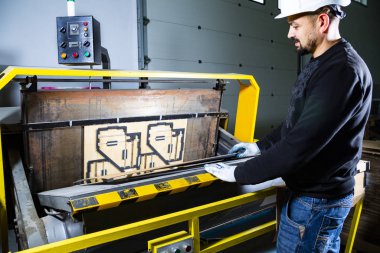 Yumruk makinesi üzerinde çalışıyorum. Karton kasklı bir fabrikada çalışan bir işçi bir karton kutuyu bir kağıda yerleştirip kesme makinesinde ölür..