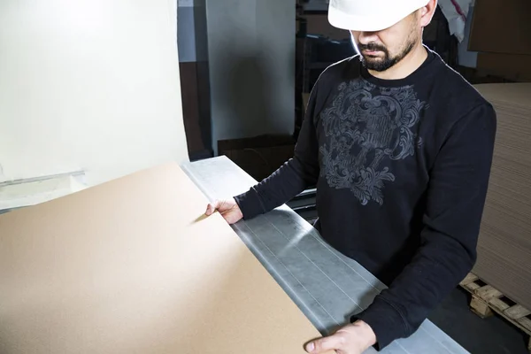 Produzione scatole di cartone. Lavoratore con un cappello duro che tiene i cartoni tra le mani . — Foto Stock