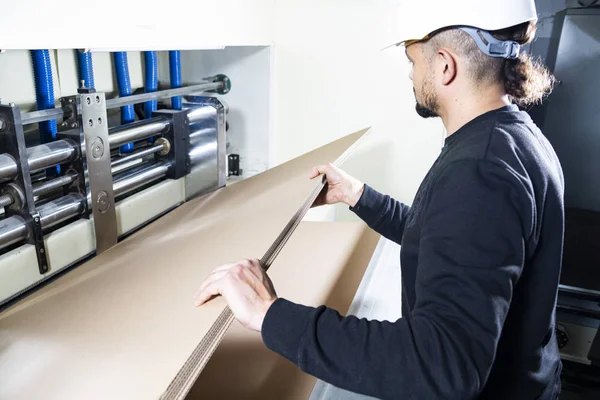 Produzione scatole di cartone. Lavoratore con un cappello duro che tiene i cartoni tra le mani . — Foto Stock