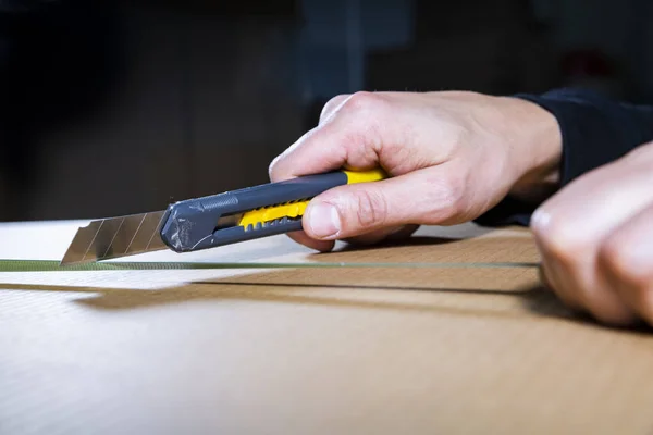 Un uomo che usa un coltello per aprire una scatola di cartone. Mano maschile che tiene uno strumento. Apertura pacchetti. Unboxing . — Foto Stock