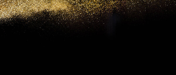 Wide view of a golden glitter scattered on a black surface. Christmas, new year, birthday, special occasions background, with a copy space.