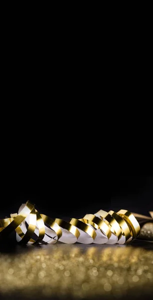 Gouden lint op een verticale, zwarte achtergrond met wazige, gouden glitter. Kerstmis, Nieuwjaar, speciale gelegenheden achtergrond, kopieerruimte. — Stockfoto