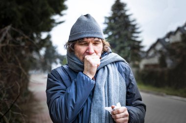 Öksüren adam caddede yürüyor. Enfeksiyon, grip, viral hastalıklar.