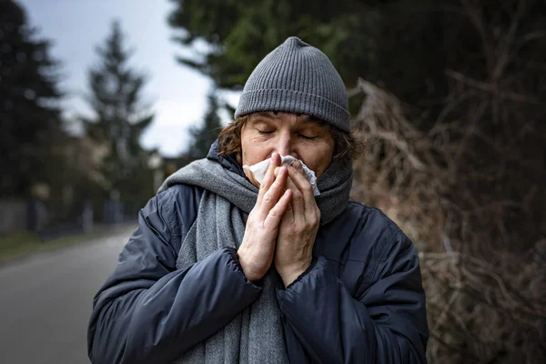 Nose wiping with a tissue. Man with a temperature, fever and runny nose, outdoor. Infection, flu, viral diseases.