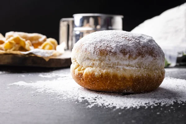 Donut covered with powdered sugar on the stony worktop.