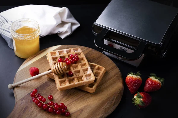 Freshly baked waffles, fruits, honey and a professional waffle iron — Stock Photo, Image