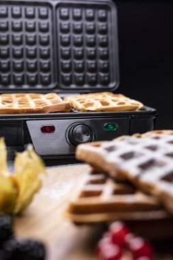 Koyu bir atölyede yeni pişmiş waffle ile waffle ızgarası..