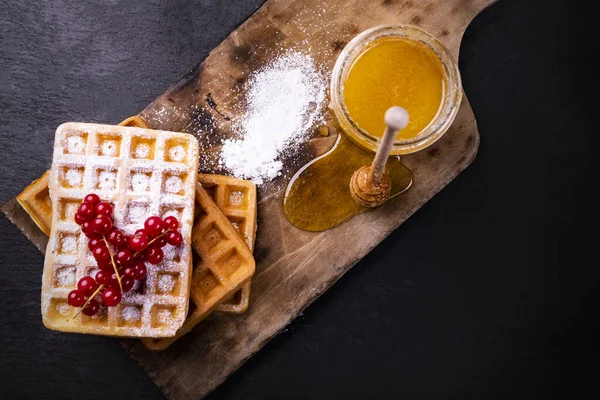 Stack of freshly baked waffles decorated with fruits, powdered sugar and honey, top view. — Stock Photo, Image