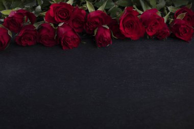 Valentine Day frame. Red roses on the upper edge on a dark background with a copyspace