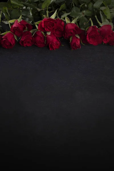 Marco de San Valentín. Rosas rojas en el borde superior sobre un fondo oscuro con un espacio de copia — Foto de Stock