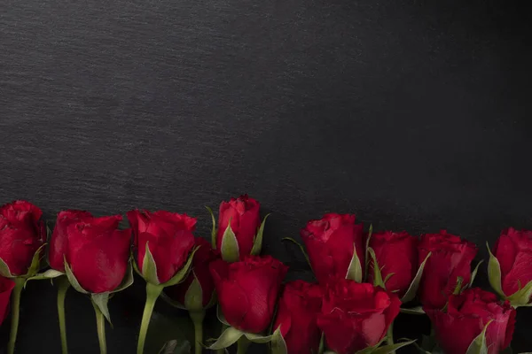 Cornice San Valentino. rose rosse sul bordo inferiore su uno sfondo scuro con un copyspace — Foto Stock