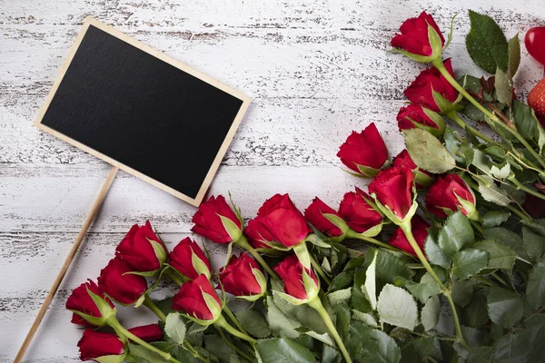 Ramo de rosas rojas en una pizarra de madera blanca con una mini pizarra con un espacio de copia — Foto de Stock