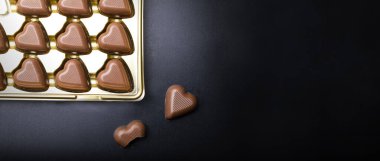 Siyah arka planda kalp şeklinde çikolatalarla dolu geniş bir pankart. Sevgililer günü hediyesi, tatlım..