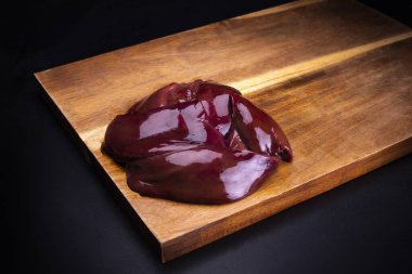 Pork livers on a wooden cutting board on a dark background.