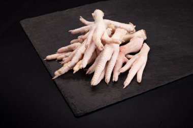 Raw chicken feet on a dark stony background.