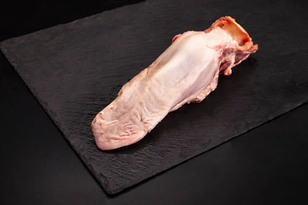 Raw pork tongue on a black background. — Stockfoto