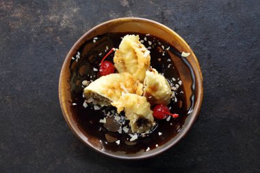 Tempura içinde kızarmış muz, badem gevreği ve maraska vişneli küçük, minimal stil, kahverengi bir kâsede. Siyah taşlı arka planda oryantal bir tatlı, üst manzara. Suşi restoranında tatlı..