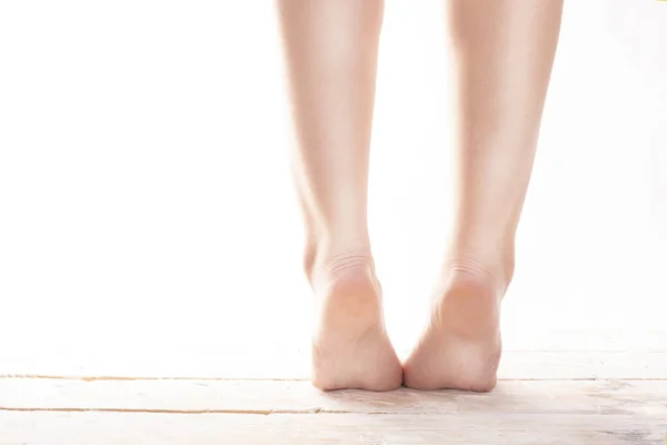 Female, healthy feet, standing on tiptoes on wood floor on a white background.