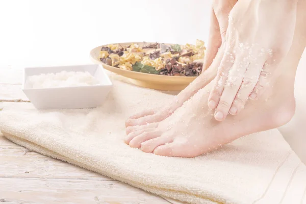 Home SPA. Young woman doing foot peeling, scrub using natural cosmetics, side view.