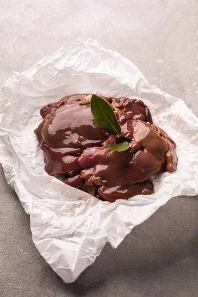 Raw chicken livers on a paper on stony countertop. Poultry, giblets.