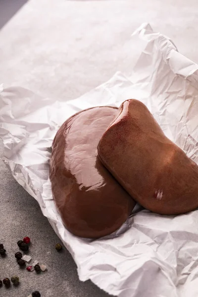 Raw pork kidneys on a paper on a stony worktop. Pig meat, organs, giblets.