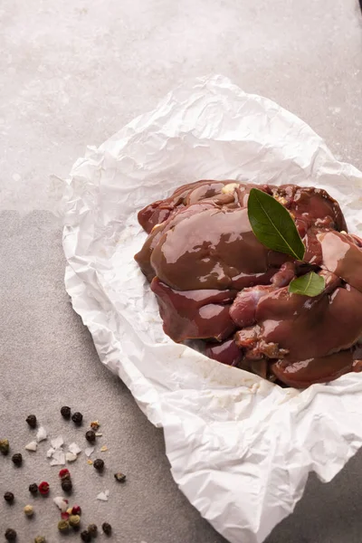 Raw chicken livers on a paper on stony countertop. Poultry, giblets, vertical view.