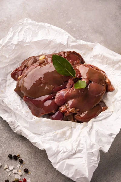 Raw chicken livers on a paper on stony countertop. Poultry, giblets, vertical view, close-up.