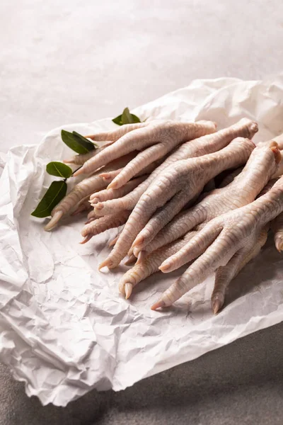 Raw chicken feet with claws on a paper on a stony worktop. Poultry parts.